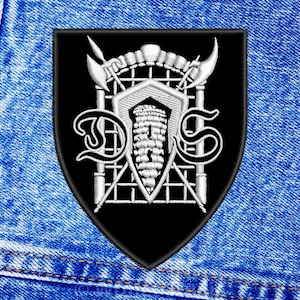 May include: Black and white embroidered patch with a shield shape. The shield features a gate with two crossed spears and the letters "D.S." in a stylized font.