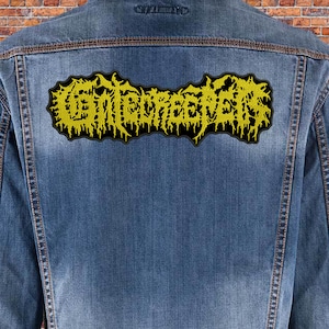 Peut inclure: Une veste en jean avec un patch brodé jaune qui dit "GHOULSCREAMER" au dos.