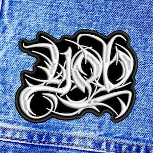 May include: White embroidered "LOL" lettering on a black patch, sewn onto a blue denim background.
