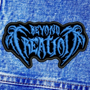 May include: Embroidered patch featuring the text "BEYOND CREATION" in a blue, gothic-style font. The patch has a black border and is displayed on a blue denim fabric. The design has a heavy metal aesthetic.