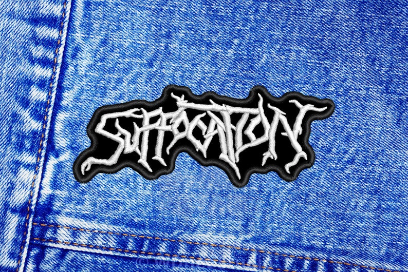 K&ouml;nnte beinhalten: Wei&szlig;er gestickter Patch auf einem blauen Jeans-Hintergrund. Der Patch zeigt das Wort "SUFFOCATION" in einer stilisierten Schrift.