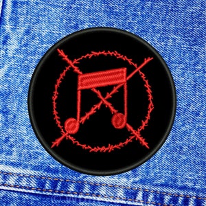Puede incluir: Un parche bordado negro y rojo con una nota musical tachada por alambre de púas. El parche es circular y tiene un borde negro.