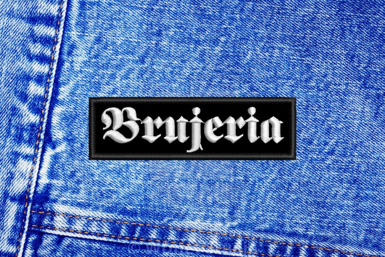 Puede incluir: Un parche negro con texto bordado en blanco que dice "Brujeria" sobre un fondo de mezclilla azul.
