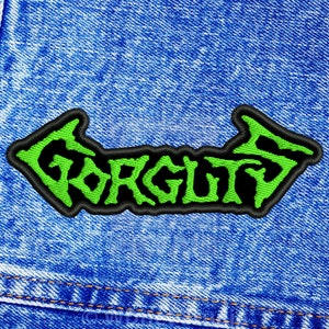 May include: Green and black embroidered patch with the word "GORGUTS" in a stylised font. The patch is sewn onto a blue denim jacket.