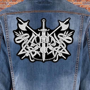 Peut inclure: Un écusson brodé blanc représentant une épée, des haches et des lances croisées. L'écusson est sur un fond noir et comporte un détail de chaîne en bas.