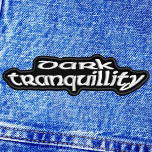 Puede incluir: Un parche bordado en blanco y negro con el texto "Dark Tranquillity" sobre un fondo de mezclilla azul.