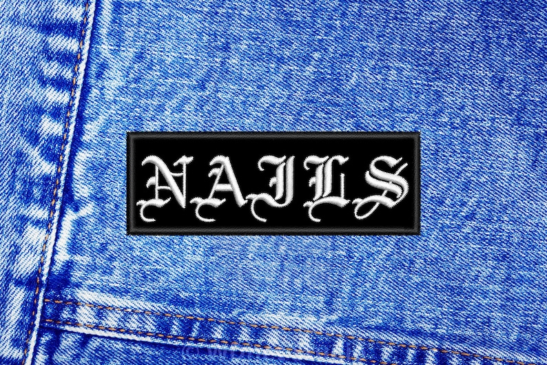 May include: Black patch with white embroidered text "NAILS" on a blue denim background.