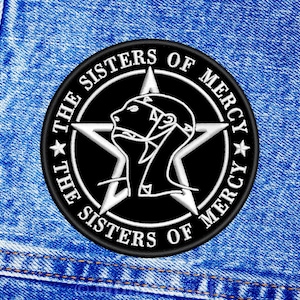 Op de afbeelding: Een zwart-witte geborduurde patch met de tekst "THE SISTERS OF MERCY" en een centrale ster. De patch heeft een gestileerde vrouwelijke figuur en is geplaatst tegen een blauwe denim achtergrond.