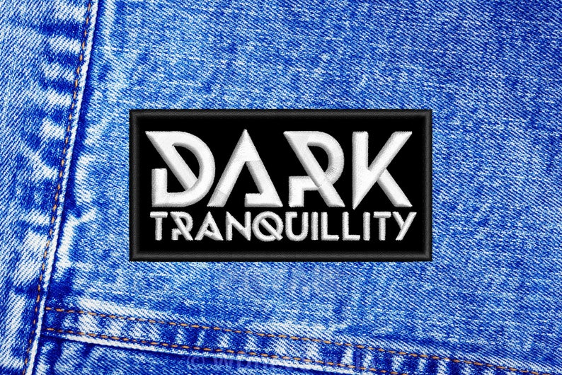 Op de afbeelding: Een zwarte patch met witte tekst die "DARK TRANQUILLITY" zegt op een blauwe denim achtergrond.