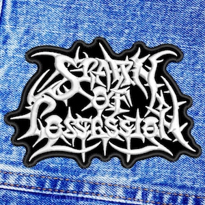 Könnte beinhalten: Ein gestickter Patch in Schwarz und Weiß mit dem Text "Scorn of a Possessed" in einer stilisierten Schrift.