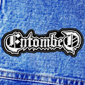K&ouml;nnte beinhalten: Wei&szlig;er gestickter Aufn&auml;her mit dem Wort "Entombed" in gotischer Schrift auf schwarzem Hintergrund. Der Aufn&auml;her ist auf eine blaue Jeansjacke gen&auml;ht.