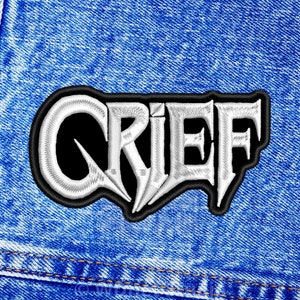May include: A white embroidered patch with the word "GRIEF" in a black outline. The patch is on a blue denim background.