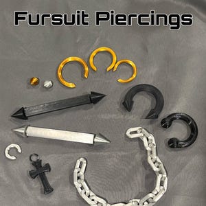 Może przedstawiać: Kolekcja Fursuit Piercings zawierająca złote pierścienie, czarne i srebrne proste pręty ze spiczastymi końcami, czarny pierścień w kształcie podkowy, srebrny łańcuszek, mały wisiorek w kształcie krzyża oraz dwie małe kuliste koraliki w kolorze złotym i srebrnym.