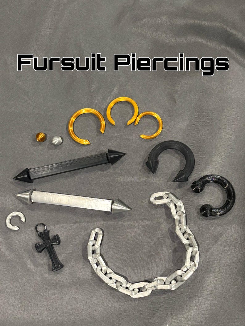Może przedstawiać: Kolekcja Fursuit Piercings zawierająca złote pierścienie, czarne i srebrne proste pręty ze spiczastymi końcami, czarny pierścień w kształcie podkowy, srebrny łańcuszek, mały wisiorek w kształcie krzyża oraz dwie małe kuliste koraliki w kolorze złotym i srebrnym.