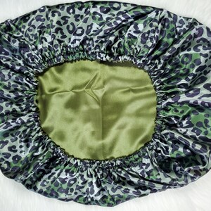 May include: Green satin sleep cap with a leopard print design. The cap has a drawstring closure and is designed to protect hair while sleeping.