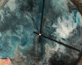 Puede incluir: Un reloj redondo con una esfera negra y agujas negras. La esfera del reloj está hecha de resina y tiene un patrón azul, blanco y gris en espiral.