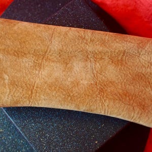 May include: A light brown leather clutch bag with a textured surface.