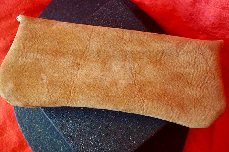 May include: A light brown leather clutch bag with a textured surface.