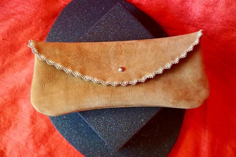 May include: A tan leather clutch bag with a scalloped edge and a silver button closure.