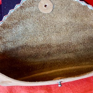 May include: A brown leather clutch bag with a scalloped edge and a beaded trim. The bag is open and the inside is lined with brown suede.