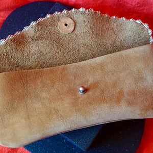May include: A brown leather clutch bag with a scalloped edge and a snap closure. The bag is open and the inside is lined with a brown fabric.