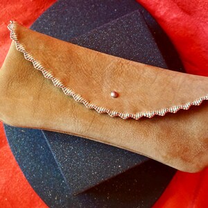 May include: A tan leather clutch with a scalloped edge and a small silver button closure.