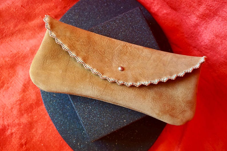 May include: A tan leather clutch with a scalloped edge and a small silver button closure.