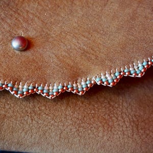 May include: Close-up of a brown leather purse with a scalloped edge trimmed with a beaded border of copper and light blue beads.