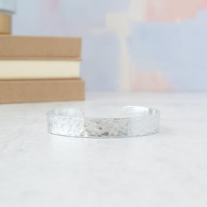 May include: A silver hammered cuff bracelet. The bracelet is made of metal and has a textured surface.