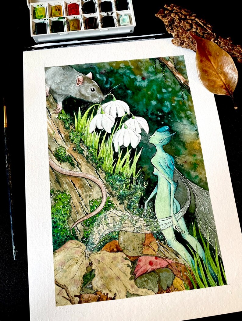 May include: Watercolor painting of a fantasy scene featuring a gray rat, a fairy, and white flowers. The fairy has blue skin and wings. The artwork is on white paper, with a palette of watercolors and a paintbrush visible.