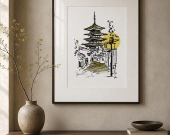May include: A framed art print featuring a black ink sketch of a multi-tiered pagoda and surrounding buildings. The illustration includes a yellow circular accent and handwritten text at the bottom left, all enclosed in a thin black frame.