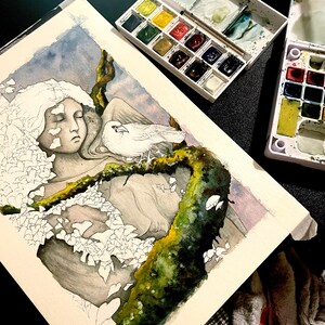 Op de afbeelding: Aquarel schilderij in uitvoering, met een serene figuur met gesloten ogen, een witte duif en een mosachtige tak. Aquarelverfpaletten met diverse kleuren omringen het kunstwerk, wat wijst op een werkruimte van een kunstenaar.