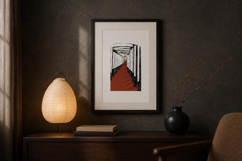 May include: A framed vertical art print featuring a black and white illustration of a tunnel of pillars with a deep red path. The artwork is displayed in a black frame with a white mat, positioned above a wooden surface with a lamp and vase.