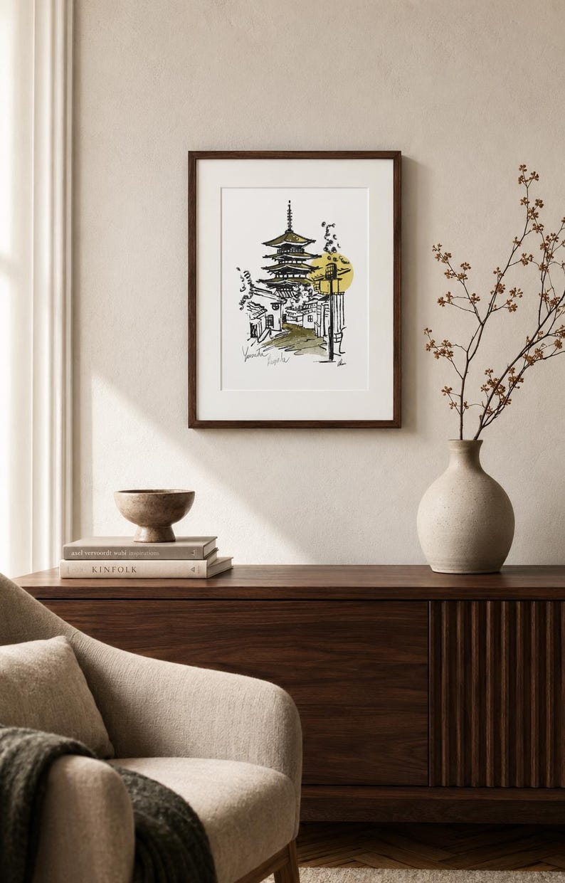 Puede incluir: Una l&aacute;mina de arte enmarcada que presenta un boceto en tinta negra de una pagoda japonesa y una escena callejera con un acento circular amarillo. El dibujo incluye texto escrito a mano en la parte inferior y se muestra en un marco de madera oscura.