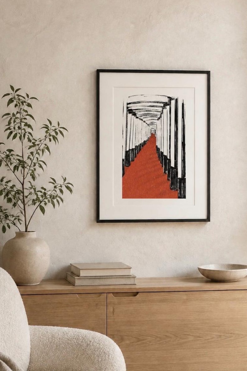May include: A framed wall art print featuring a black and white ink-style illustration of a long corridor lined with vertical pillars, with a vibrant red path extending through the center, enclosed in a simple black frame with a white mat border.