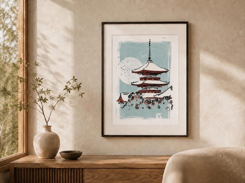 May include: A framed wall art print featuring a multi-tiered pagoda in shades of red and white against a light blue background. A large white circular moon is visible behind the structure, with dark floral elements at the base of the pagoda.