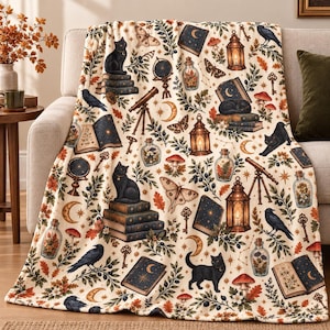 Peut inclure: Un plaid couleur crème orné d'un motif répétitif de chats noirs, corbeaux, papillons de nuit, lanternes lumineuses, télescopes, livres ouverts, croissants de lune, clés et champignons avec des feuilles d'automne et des tiges botaniques.