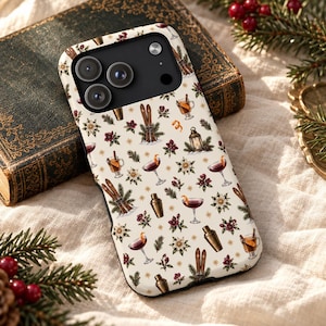 May include: A smartphone case with a cream-coloured background featuring a repeating pattern of winter-themed illustrations including vintage skis, cocktail glasses with orange peels, metal cocktail shakers, lanterns, pine branches, and berries.