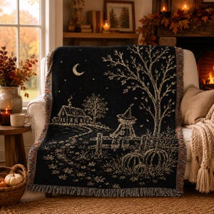 Peut inclure: Un plaid tissé noir présentant une scène détaillée d'un épouvantail assis sur une clôture, une maison, un croissant de lune et des citrouilles. Le motif est réalisé en fil clair sur un fond sombre avec des bords à franges.