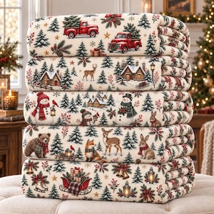 Könnte beinhalten: Ein Stapel aus fünf gefalteten cremefarbenen Decken mit einem wiederkehrenden Weihnachtsmuster. Das Design zeigt rote Pickups, verschneite Hütten, Schneemänner, Bären, Hirsche, Füchse, Hasen, Tannenbäume, Laternen und einen roten Schlitten mit Geschenken.