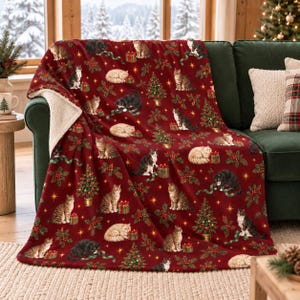 May include: A deep red throw blanket with a white sherpa lining, featuring a repeating pattern of various cats, decorated Christmas trees, holly sprigs, and gift boxes. The cats are depicted in sitting, lying, and playing positions.