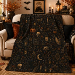May include: A black throw blanket featuring a detailed pattern of orange and gold Halloween motifs, including pumpkins, skulls, a Book of Shadows, potion bottles, a crescent moon, a black cat, a raven, a ghost, and various botanical elements.