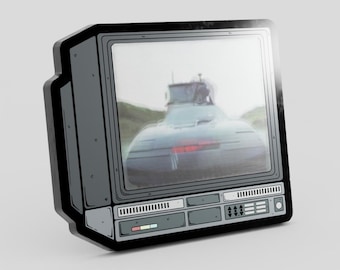 May include: A gray, rectangular enamel pin shaped like a vintage television set. The screen displays a blurry image of a dark car with a glowing red light on the front bumper. The frame features black outlines, control buttons, and vents.