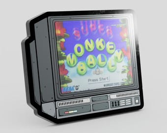 Może przedstawiać: Czarno-szara emaliowana przypinka w kształcie telewizora w stylu vintage. Ekran wyświetla tytuł gry Super Monkey Ball żółtymi literami na niebieskim tle z czerwonymi kwiatowymi akcentami oraz napis Press Start na dole.