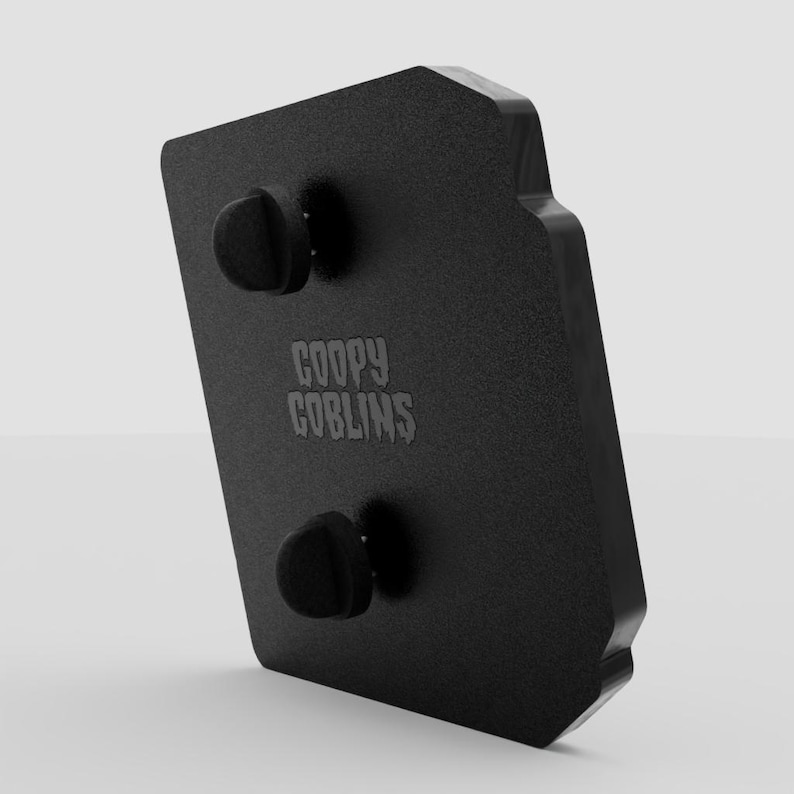 May include: A black enamel pin with the text "GOOPY GOBLINS" in a stylized font. The pin has two black posts on the back for attachment. The pin is rectangular with a unique shape.