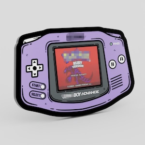 May include: A purple and black Game Boy Advance sticker featuring a game screen with the text "RUBY VERSION" and a graphic of a creature. The sticker has a black outline and includes the text "BOY ADVANCE".