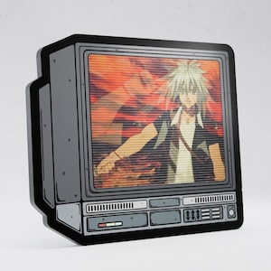May include: A flat, rectangular decorative object shaped like a vintage television set. The screen displays a stylized anime character with spiky white hair against a red background. The frame is black and gray with detailed control panel graphics.