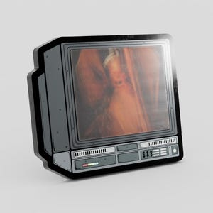 Pode incluir: Um alfinete de televisão retrô cinza e preto com uma tela exibindo uma imagem borrada. O alfinete tem um design detalhado com botões e um alto-falante. A tela mostra uma pessoa com um fundo borrado.