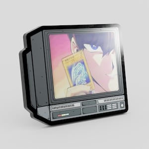 Puede incluir: Un pin negro y gris con forma de televisor retro. La pantalla muestra un personaje sosteniendo una tarjeta coleccionable dorada con un dragón azul. El pin tiene botones detallados y un diseño de altavoz.