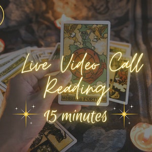 May include: A hand holds a tarot card with a golden wheel of fortune design. The card is surrounded by other tarot cards and candles. The text "Live Video Call Reading 15 minutes" is written in gold letters on the image.